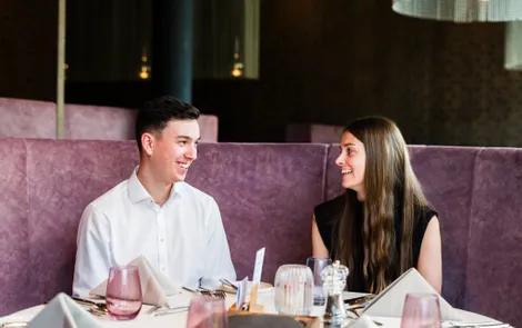 Zweisamkeit im Good Life Resort Lächelndes Paar sitzt an einem Tisch in modernem Restaurant mit violetten Sitzecken